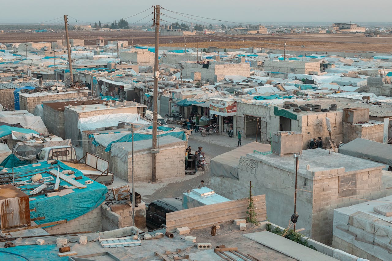 about-us A broad aerial view of a refugee camp with makeshift shelters and blue tarps in an urban area.