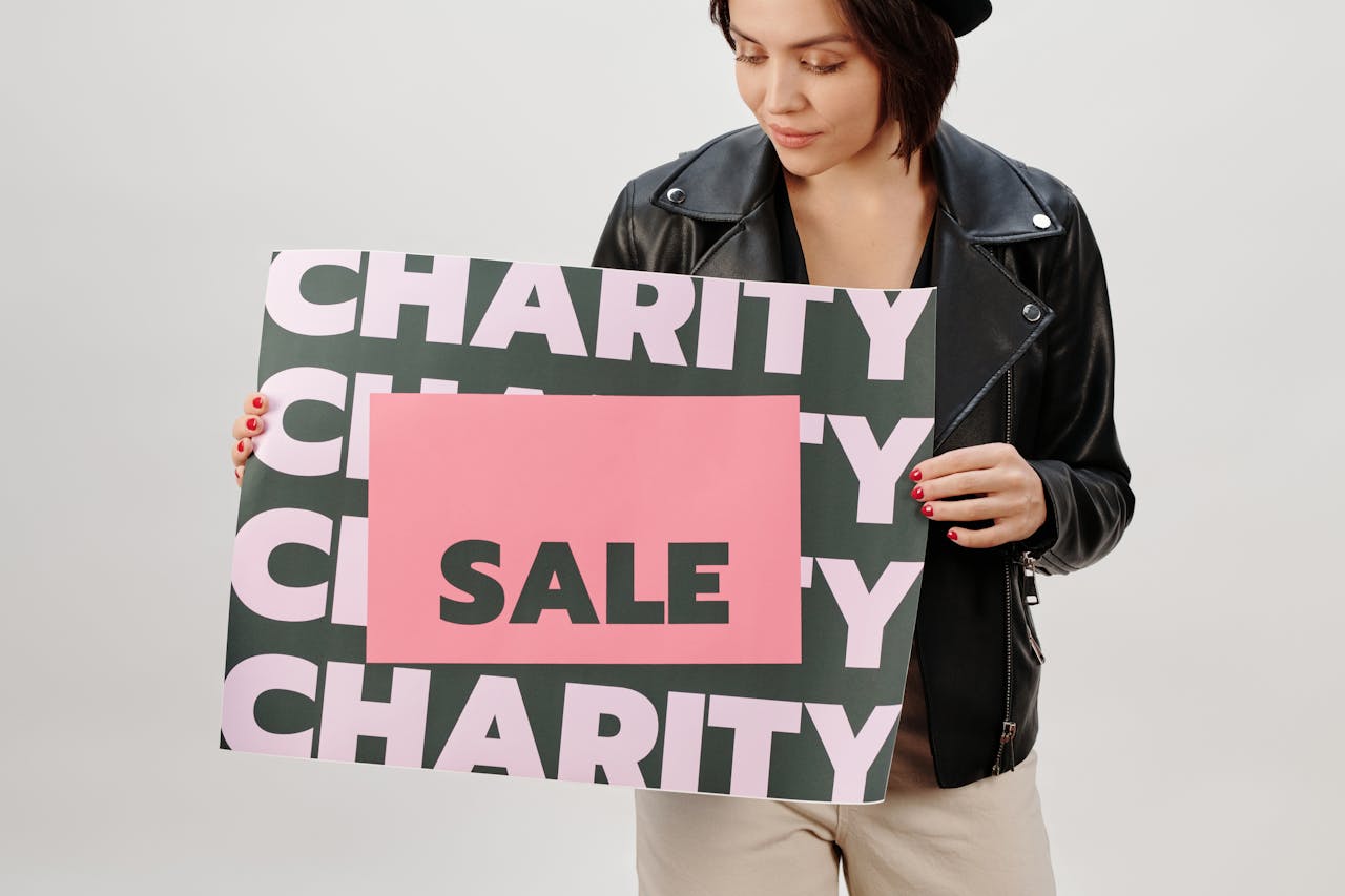 Woman holding a charity sale sign in a studio setting.